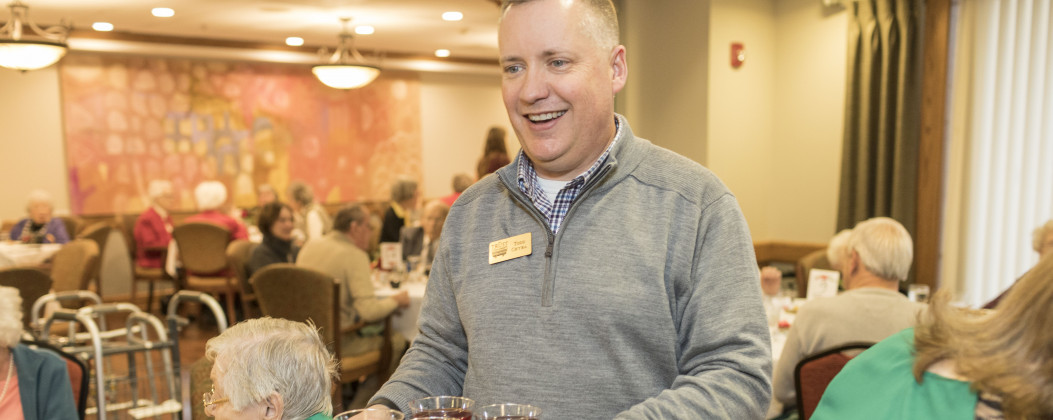 Smiling man serving holiday beverages at a nursing home party